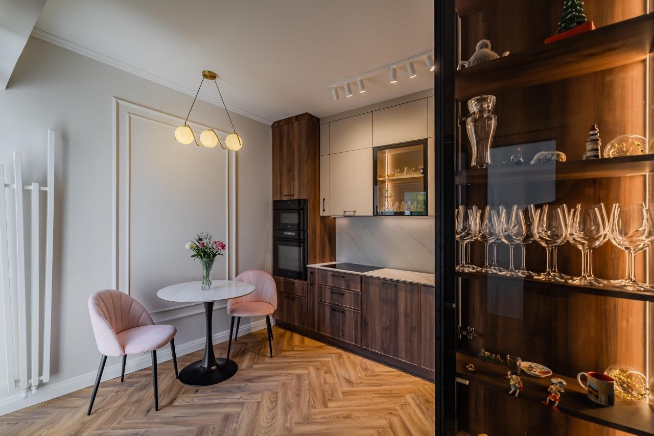 Compact kitchen and dining corner in the Gimnasticii apartment with warm wood cabinetry, glass-fronted storage and a pendant over the table