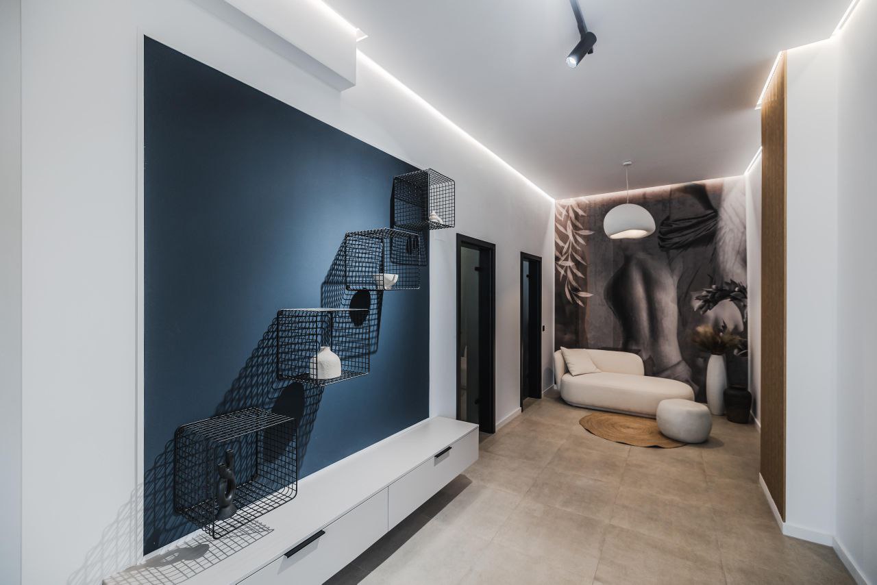 Adrett Beauty-Med hallway with large-format flooring, dark blue accent panel, light seating and discreet perimeter lighting