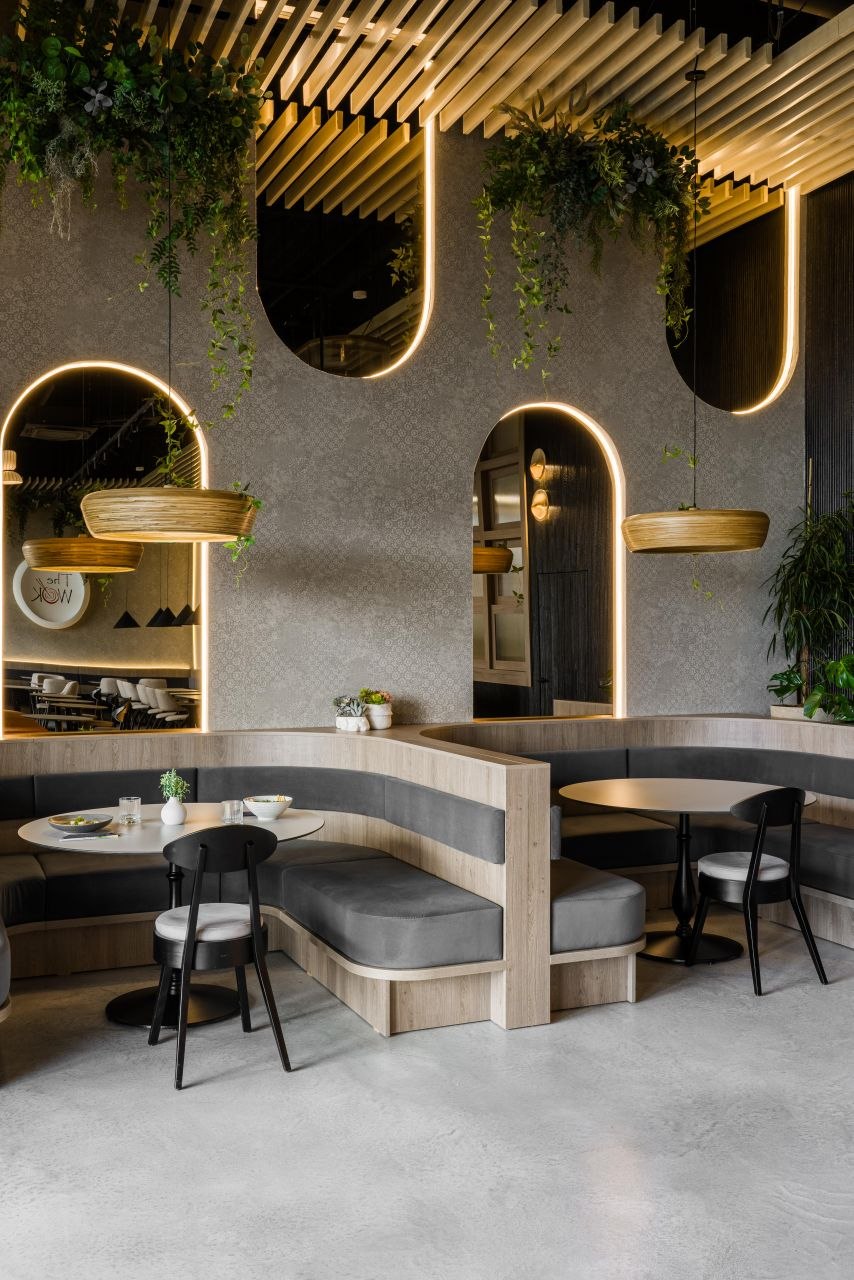 The Wok — a pale-wood banquette, matte tables, textured walls and warm-lit arches where reflections stay restrained and the room gains depth.